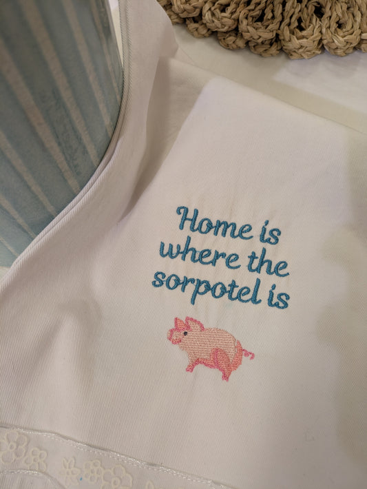 Embroidered text and pig design on a white tea towel 